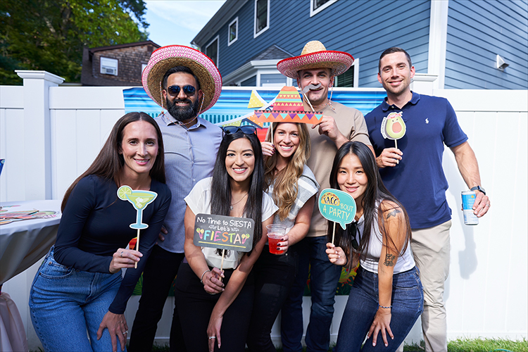 Seven people posing for the camera with colorful drinks and hats.