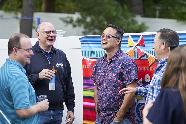 Group of four people talking a laughing with colorful decorations behind on white fence.