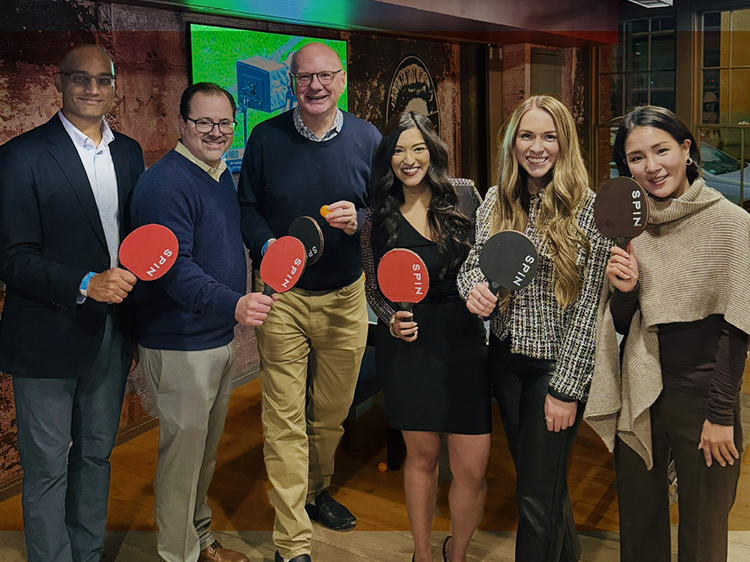 Group of people holding ping pong paddles and smiling.